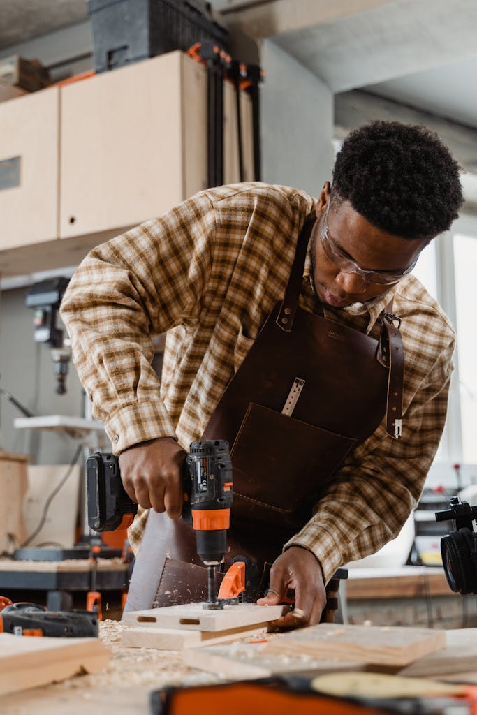 A focused carpenter using a drill in a woodworking workshop, showcasing craftsmanship.